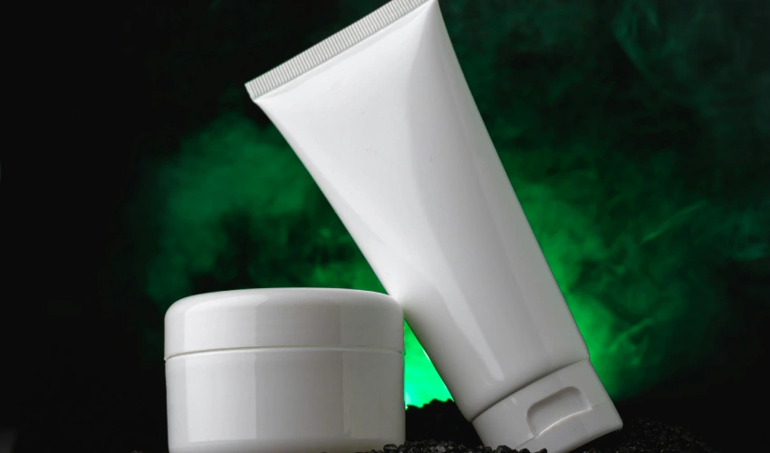 Cannabis cream tube and jar on dark surface with green background