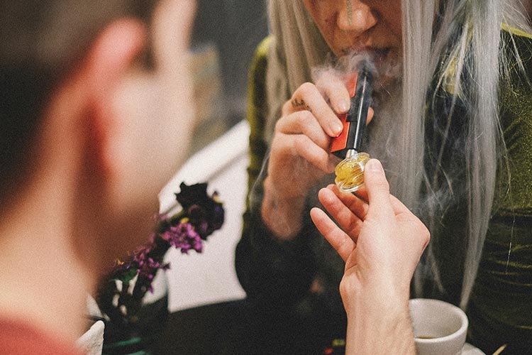 Person holding cannabis concentrate while another uses a dab tool